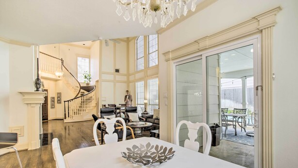 A spacious living area with a dining table, white chairs, and a chandelier. A staircase leads to another level, and there is a glass door leading to an outdoor patio. - Han Solo's Hideout Luxe Houston Home w/ Pool! (Houston)