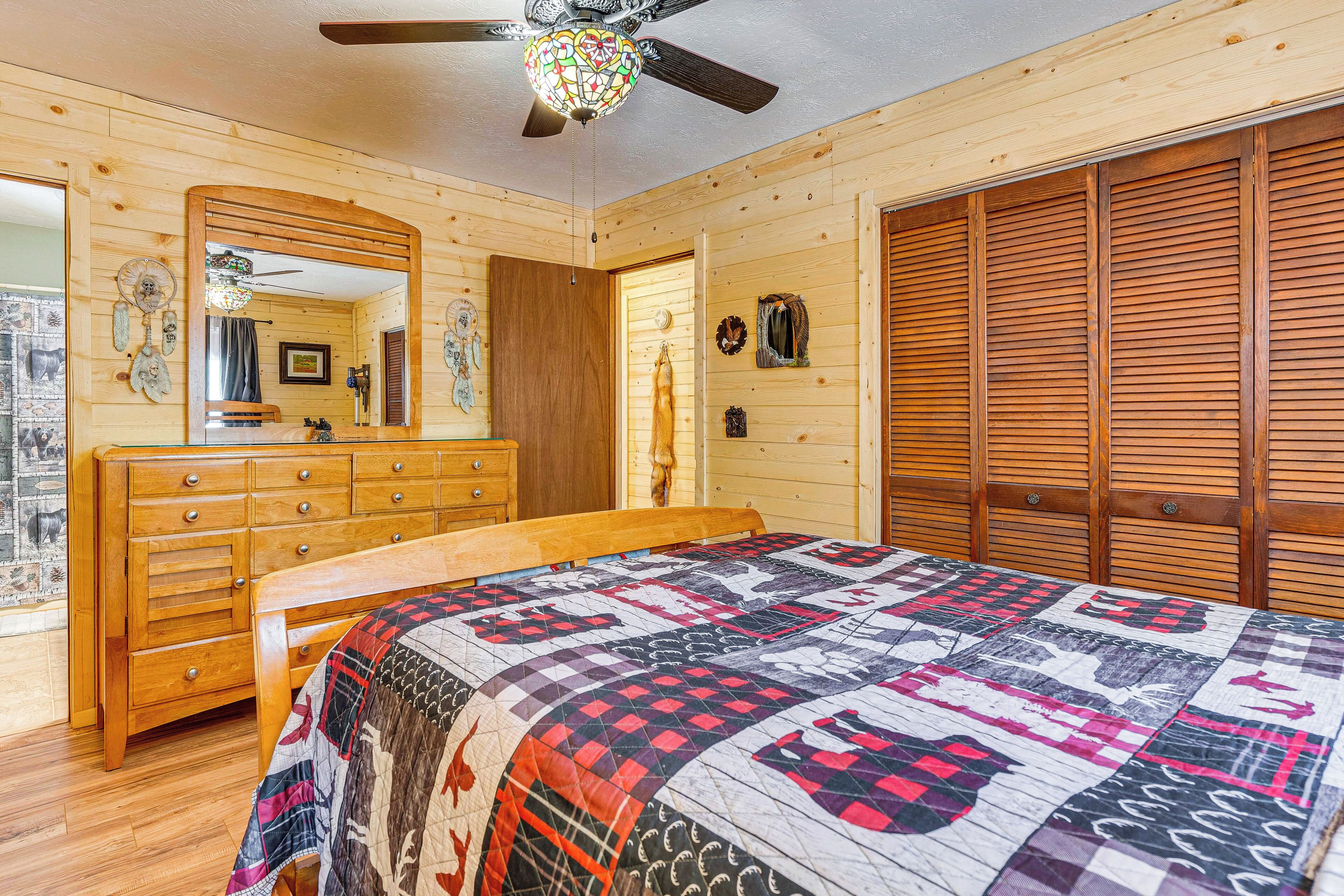 A wooden cabin bedroom with a bed, dresser, and closet.