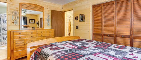 A wooden cabin bedroom with a bed, dresser, and closet.