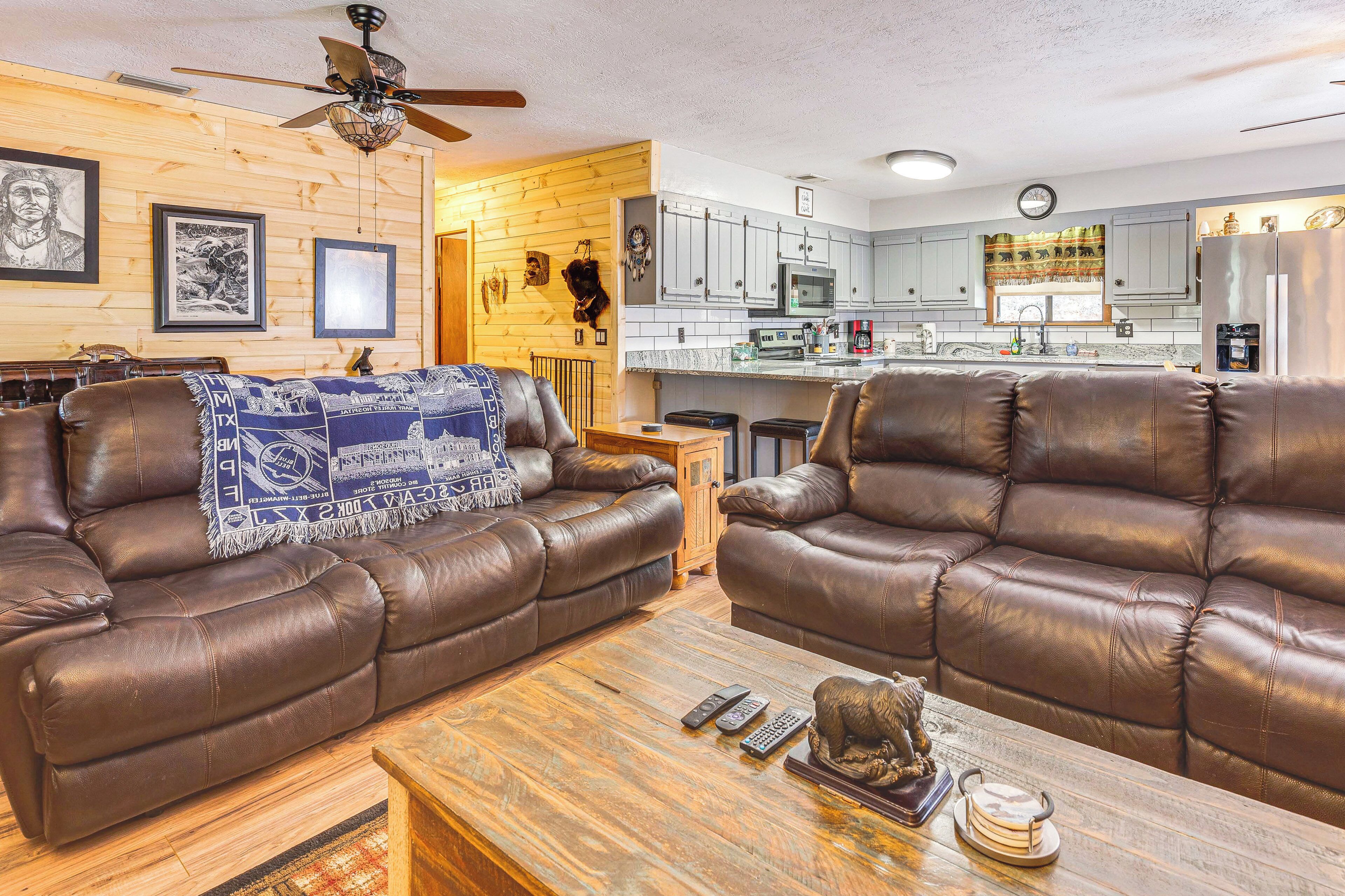 A living room with two brown leather sofas, a wooden coffee table, and a kitchen area with grey cabinets and a refrigerator.