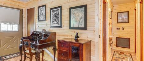 Un interior de madera con un piano, un armario y obras de arte enmarcadas en las paredes.