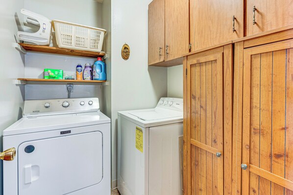A laundry room with a washing machine, dryer, wooden cabinets, and shelves with laundry supplies. - Murphy Cabin w/ Deck, Grill & Private Pond! (Murphy)