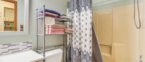 A bathroom with a toilet, sink, shower, and a towel rack with folded towels.