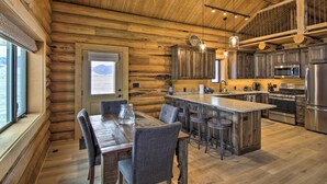 A rustic cabin interior with a wooden dining area, kitchen with modern appliances, and a large window overlooking a mountainous landscape. - Stunning Mountain Views: Livingston Cabin w/ Deck! (Livingston)