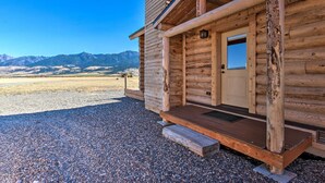 A log cabin with a wooden porch and a door, set against a mountainous backdrop. - Stunning Mountain Views: Livingston Cabin w/ Deck! (Livingston)