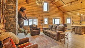 Ein Blockhaus-Interieur mit Steinwand, einer Bärenstatue, Ledermöbeln und einer Küchenzeile.