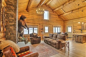 L’intérieur d’une cabane en rondins, avec un mur en pierre, une statue d’ours, des meubles en cuir et un coin cuisine.
