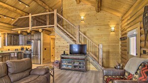 A log cabin interior with a wooden staircase, a living room with leather sofas, a kitchen with stainless steel appliances, and a television on a wooden stand. - Stunning Mountain Views: Livingston Cabin w/ Deck! (Livingston)