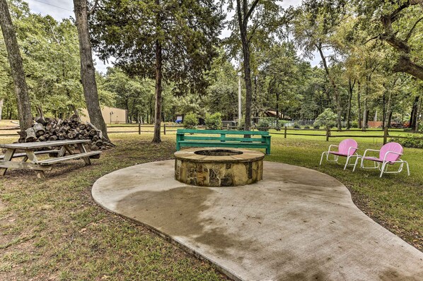 A park with a circular fire pit, a green bench, and picnic tables.