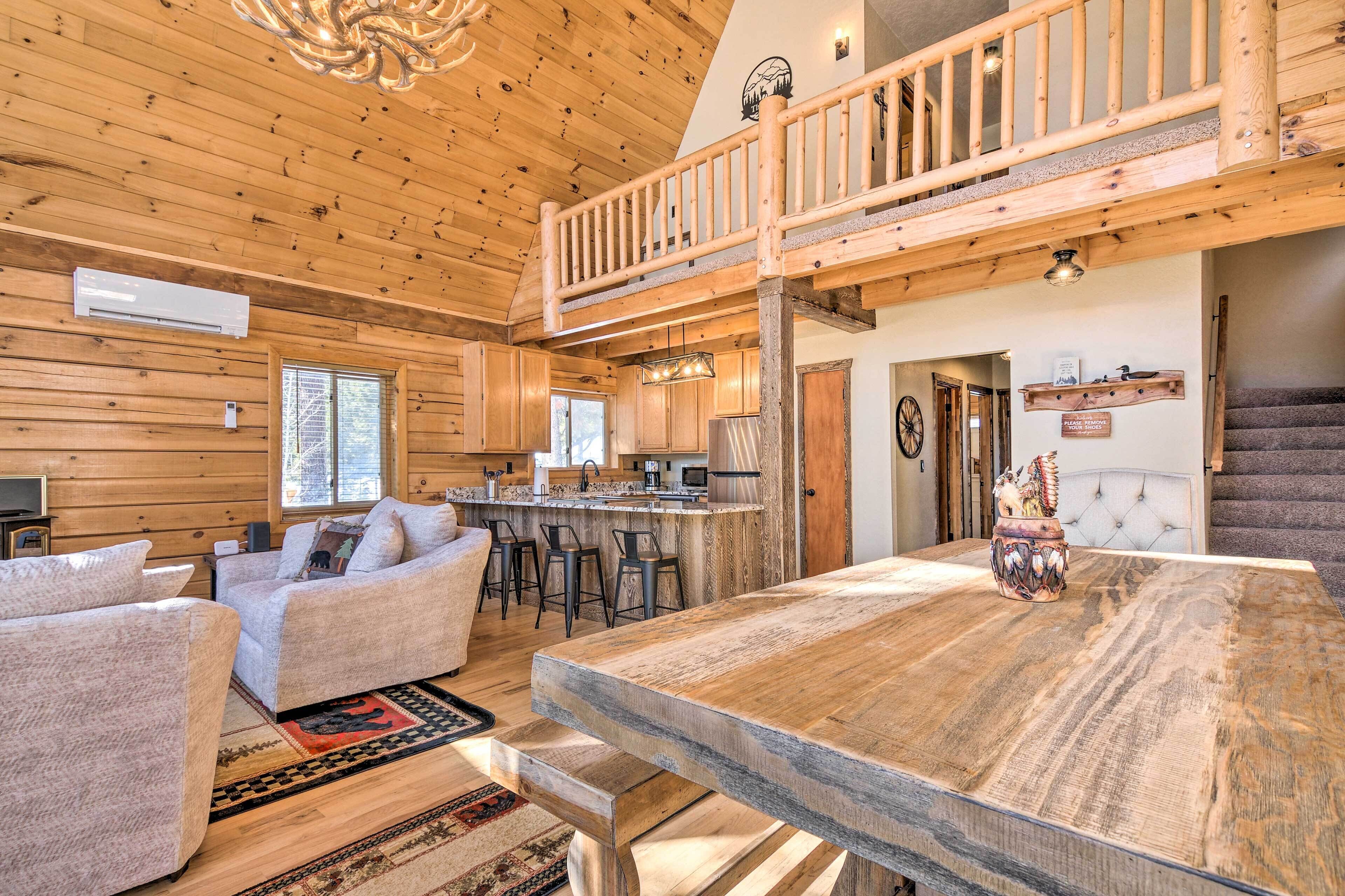 A spacious log cabin interior with a dining area, kitchen, and a second-floor balcony.