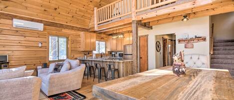 A spacious log cabin interior with a dining area, kitchen, and a second-floor balcony.