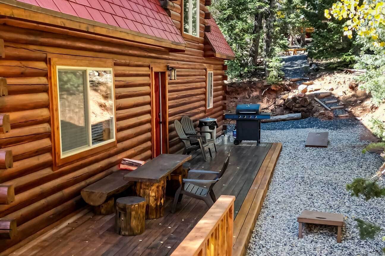 Una cabaña de troncos con terraza, asientos exteriores y una parrilla.