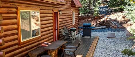 Una cabaña de troncos con terraza, asientos exteriores y una parrilla.