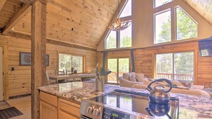 Ein Holzblockhaus-Interieur mit einer Küche, die einen Edelstahlherd, einen Essbereich mit Tisch und Stühlen sowie große Fenster mit Tageslicht umfasst.