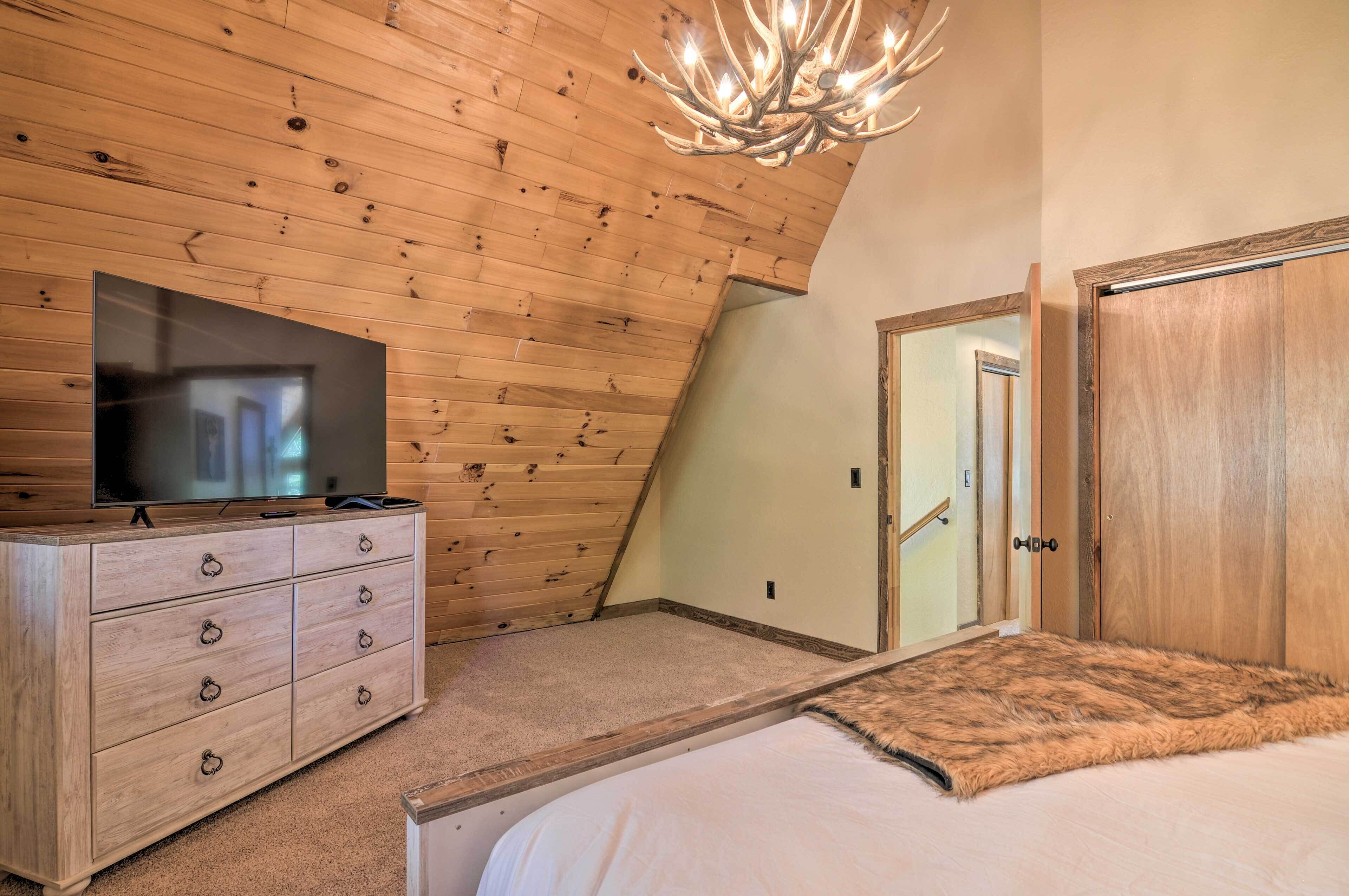 A bedroom with a sloped ceiling, wooden walls, a television on a dresser, a fluffy rug, and a door with a wooden frame.