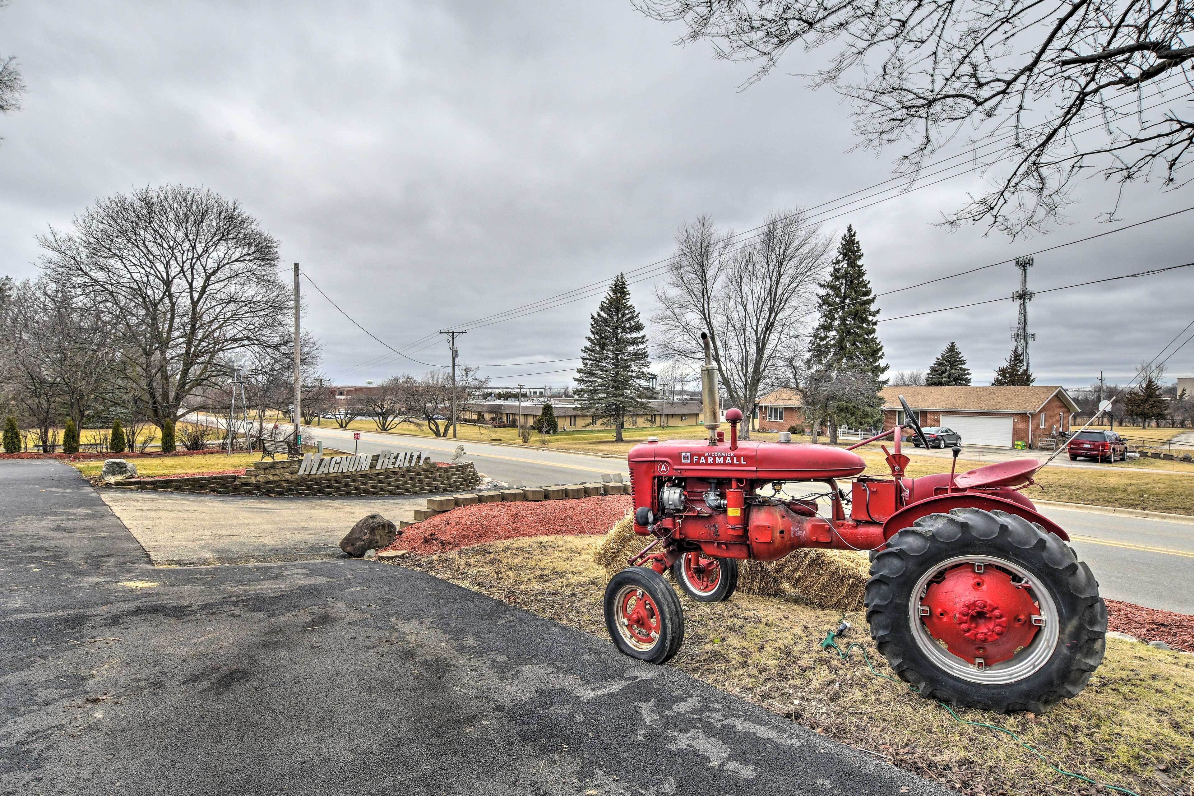 A red tractor parked on a driveway with a stone wall and a grassy area in the background.