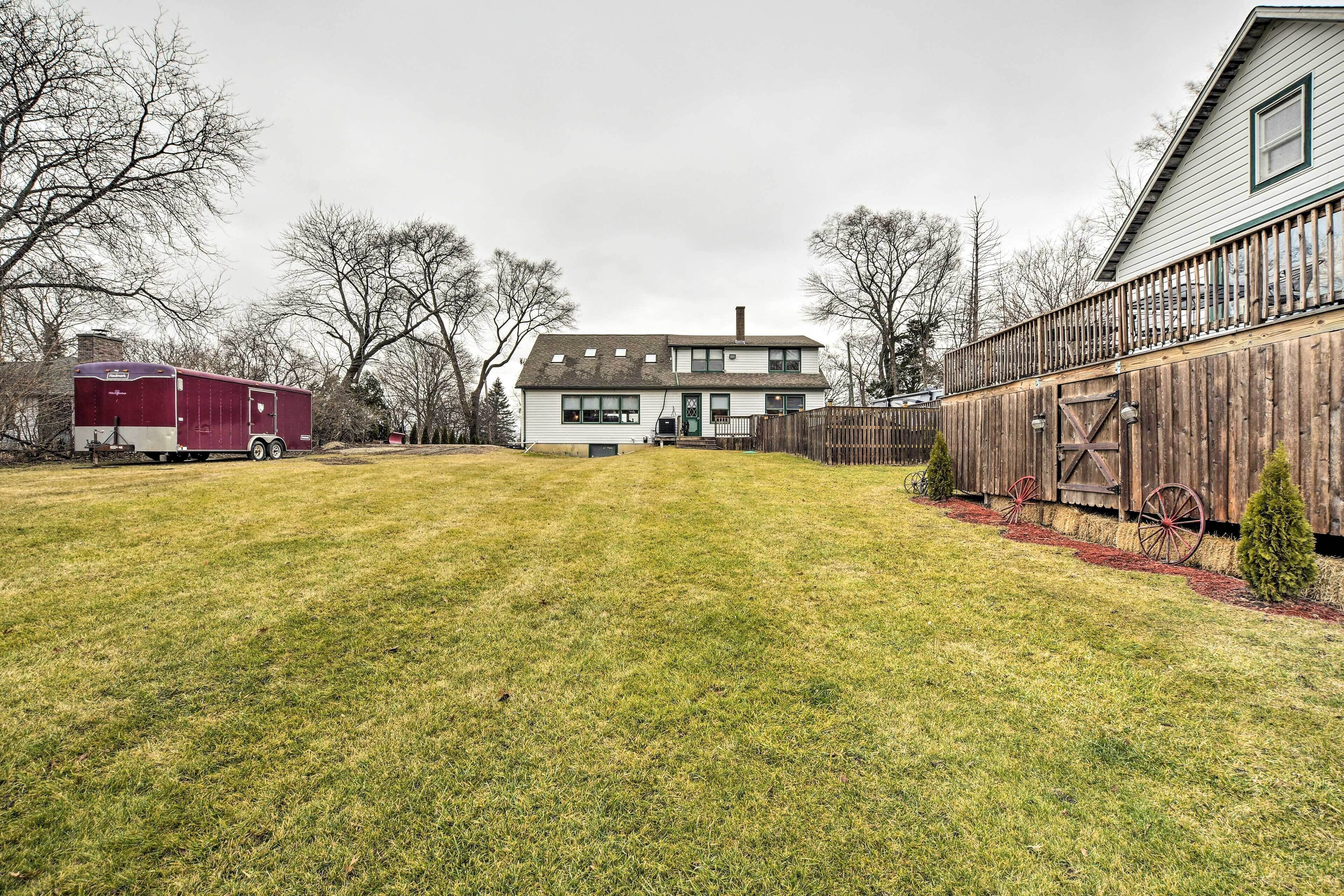 A two-story house with a front yard, a wooden fence, and a red trailer in the background.