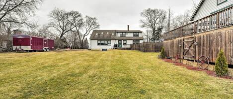 A two-story house with a front yard, a wooden fence, and a red trailer in the background.