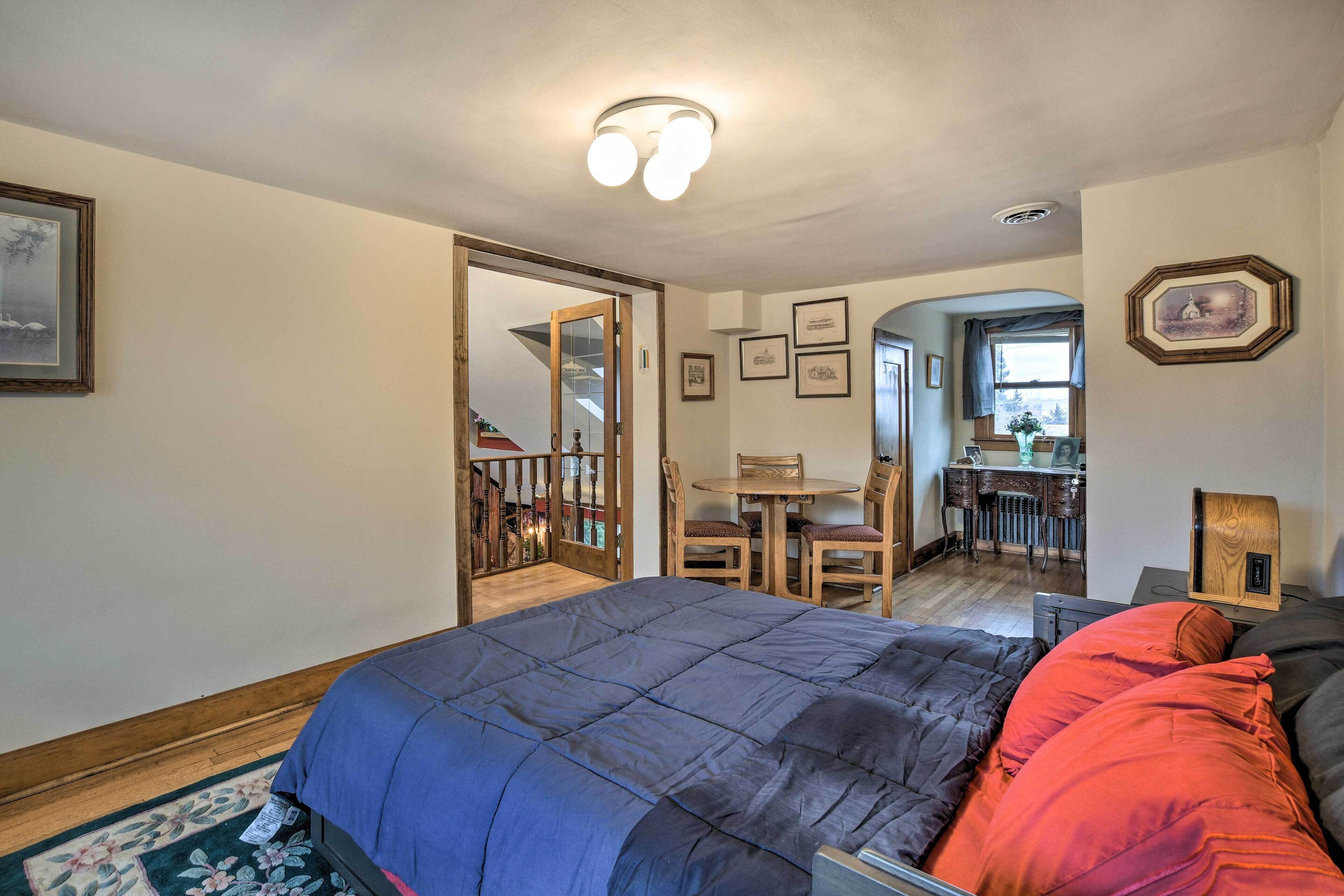 Un dormitorio con una cama grande, un escritorio y una silla. Hay una puerta que conduce a otra habitación.