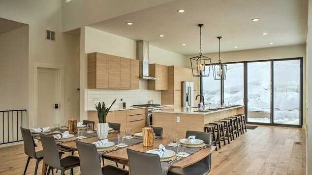 Une cuisine moderne avec des meubles en bois, un îlot central et un coin repas comprenant une longue table et des chaises.