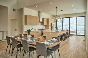 A modern kitchen with wooden cabinets, a central island, and a dining area with a long table and chairs. - Mtn-view Home w/ Hot Tub, 9 Mi to Vail Resort (Avon)
