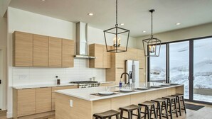 Une cuisine moderne avec des meubles en bois, un grand îlot central doté de tabourets et un éclairage suspendu.
