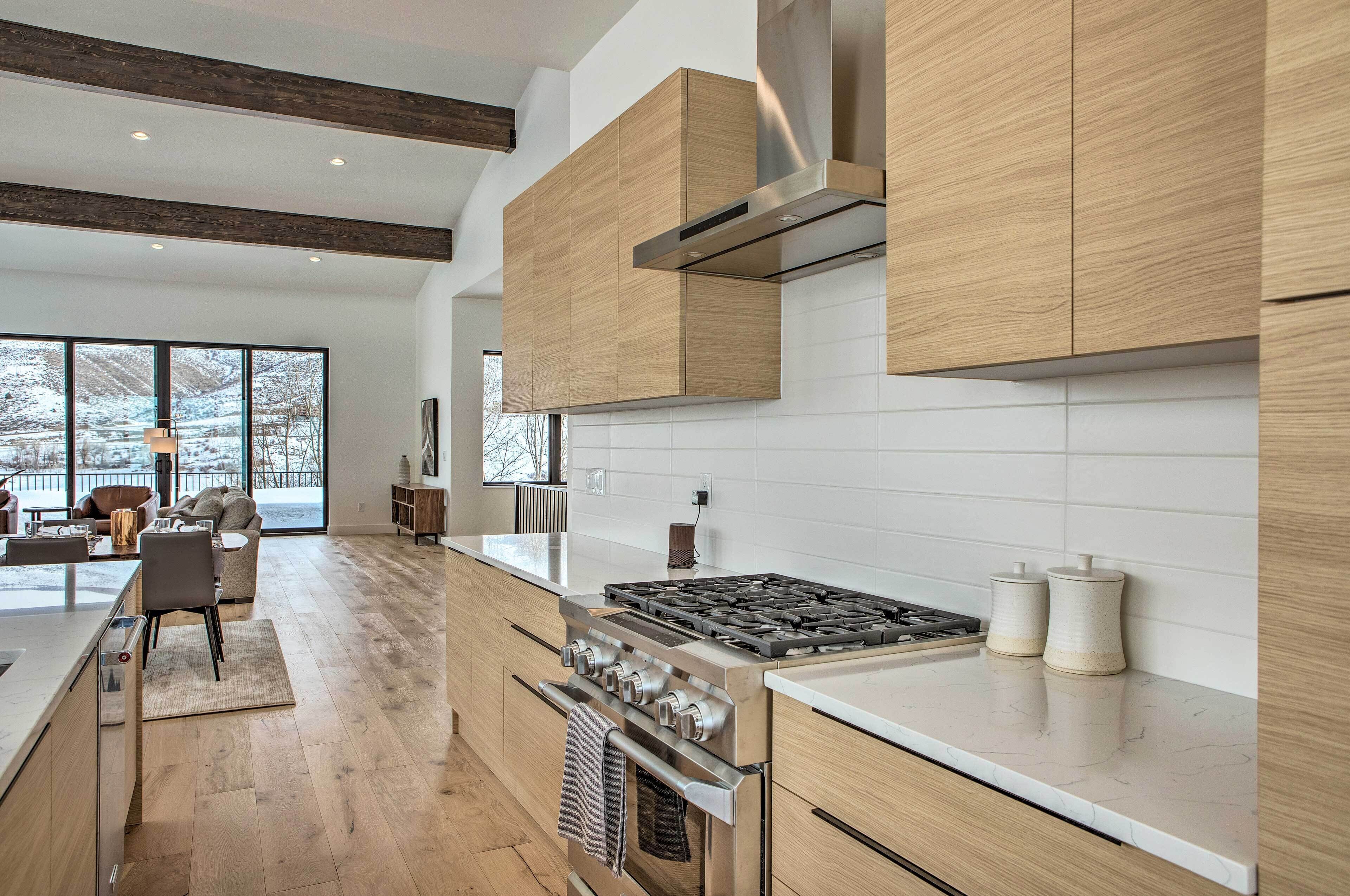 A modern kitchen with wooden cabinets, a stainless steel stove, and a large window overlooking a snowy landscape.