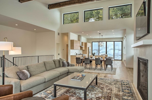 A spacious living area with a sectional sofa, a coffee table, and a fireplace. There is a dining area with a table and chairs, and a kitchen in the background.