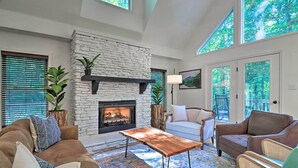 A cozy living room with a stone fireplace, comfortable seating, and large windows offering a view of the outdoors. - 2 Mi to Sapphire Resort: Home w/ Hot Tub & Games! (Sapphire)