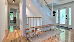 A spacious hallway with wooden flooring, a wooden bench, a basket with colorful cushions, and a staircase with white railings. - 2 Mi to Sapphire Resort: Home w/ Hot Tub & Games! (Sapphire)