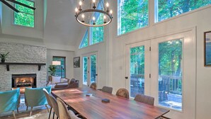 A spacious dining area with a long wooden table, surrounded by chairs, a fireplace, and large windows offering views of greenery. - 2 Mi to Sapphire Resort: Home w/ Hot Tub & Games! (Sapphire)