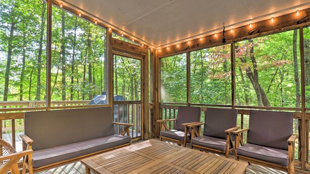 A covered outdoor seating area with wooden furniture and large windows overlooking a forest. - 2 Mi to Sapphire Resort: Home w/ Hot Tub & Games! (Sapphire)