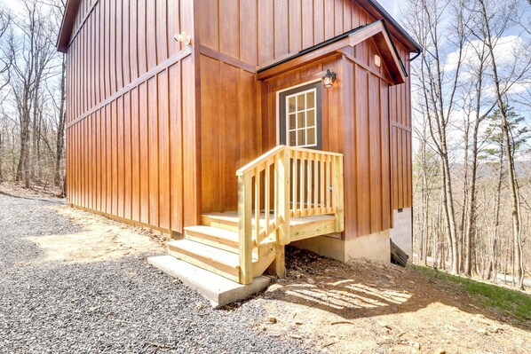 A wooden cabin with a wooden staircase leading to a door, surrounded by trees.