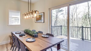 A dining area with a wooden table, chairs, a hanging light fixture, and a view of a deck and trees through large windows. - Mtn Retreat w/ EV Charger Near Bryce Ski & Golf (Mount Jackson)