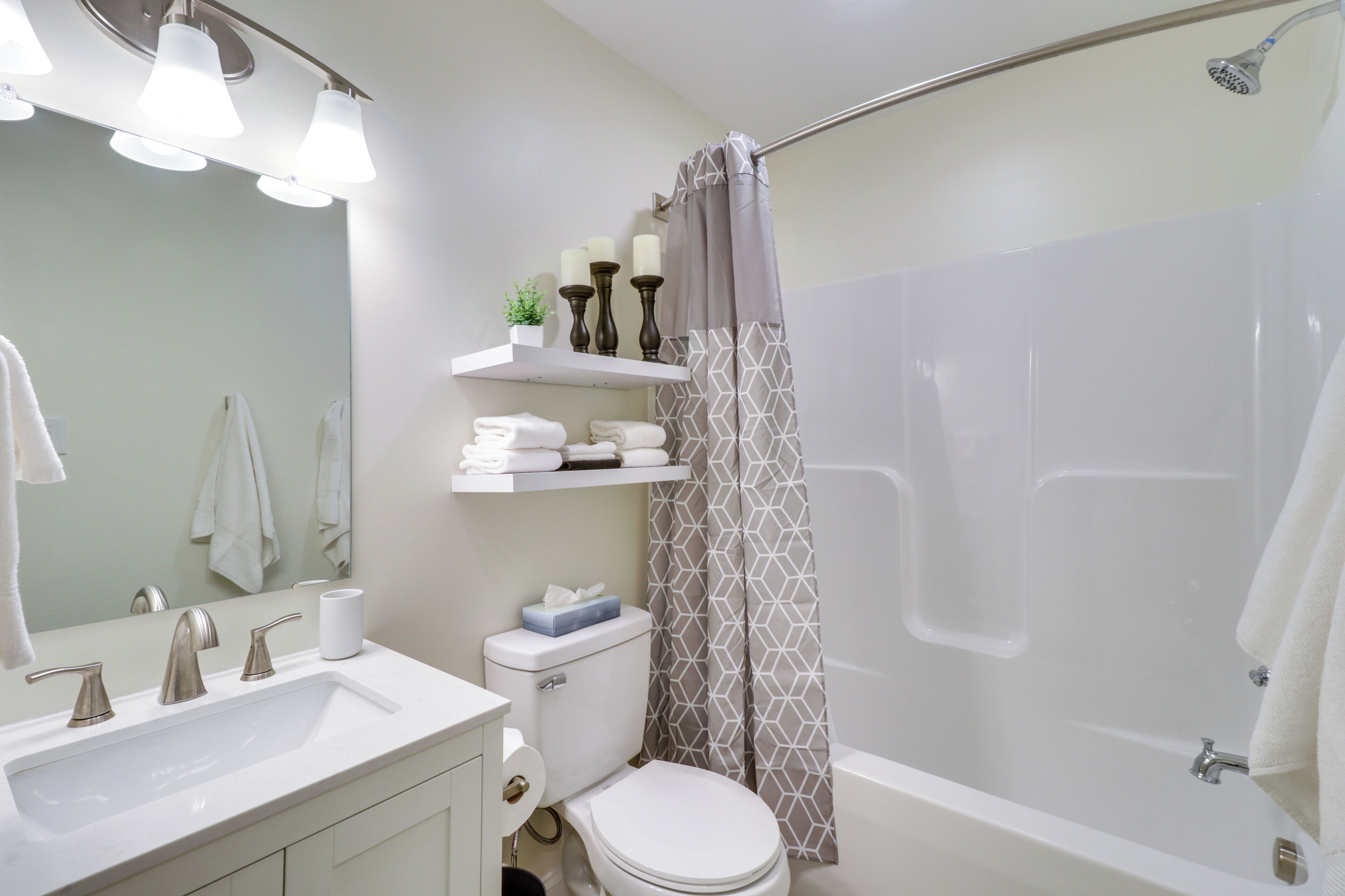A bathroom with a white sink, mirror, and toilet. There is a shower curtain and a towel rack with towels.