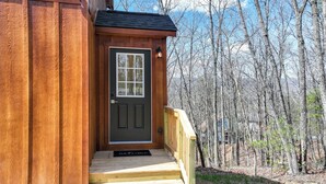 A wooden cabin with a dark front door, a small porch, and a view of a forested area. - Mtn Retreat w/ EV Charger Near Bryce Ski & Golf (Mount Jackson)