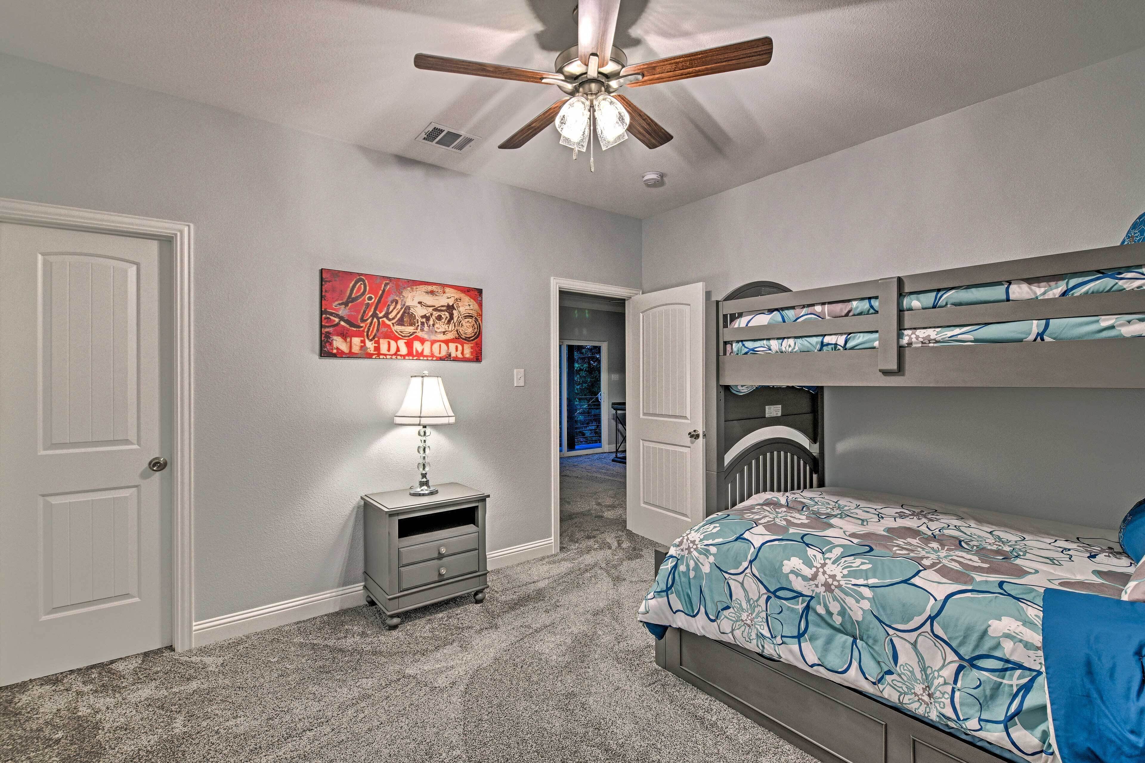 A bedroom with a bunk bed, a nightstand with a lamp, a ceiling fan, and a poster on the wall.