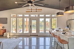 A modern kitchen with a large island, bar stools, and a view of the outdoors through large windows.