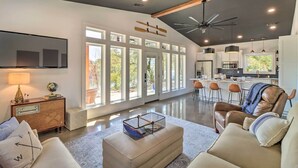 A spacious living room with a large TV, comfortable seating, and a kitchen area with bar stools. - Modern Norfork House w/ Patio on White River! (Norfork)