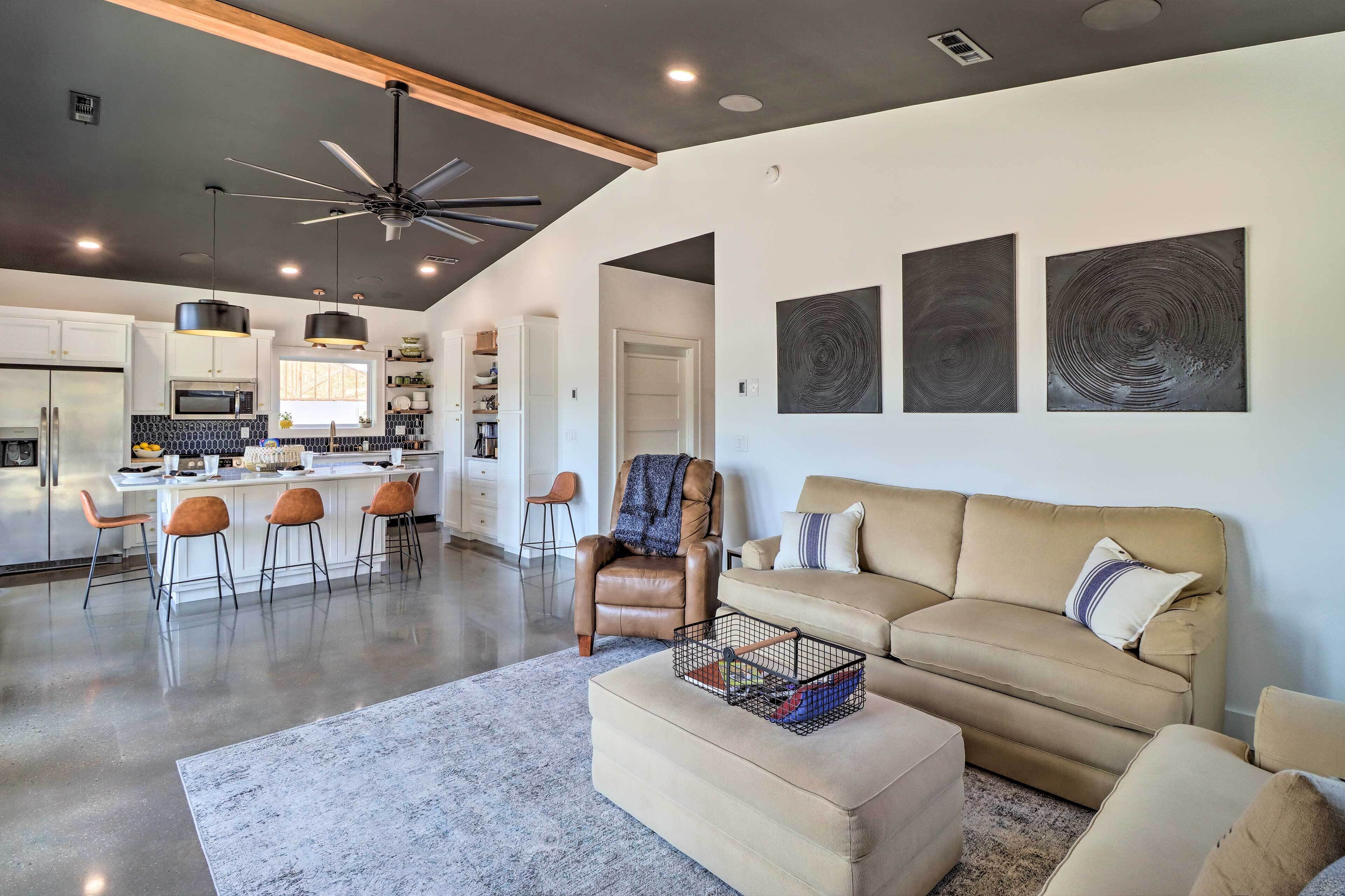 A modern kitchen with a central island, bar stools, and a ceiling fan.