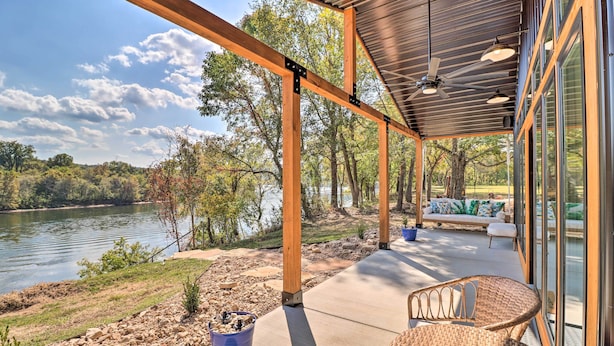 A covered outdoor area with a view of a lake, wooden beams, and a seating area with cushions. - Modern Norfork House w/ Patio on White River! (Norfork)