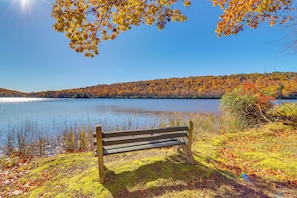 A bench by a lake with autumn foliage and a clear sky.