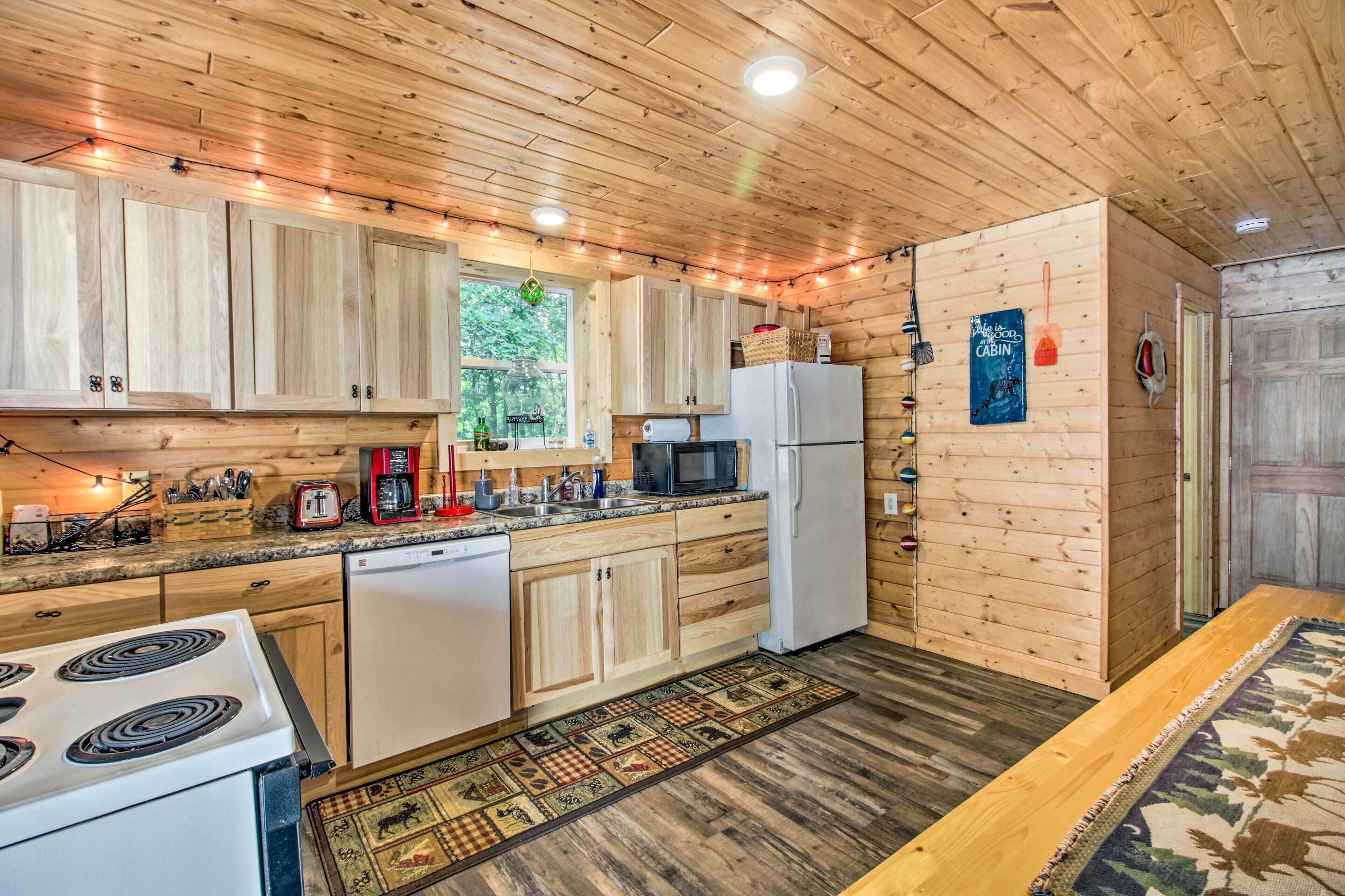 A wooden cabin kitchen with a stove, refrigerator, microwave, and wooden cabinets.