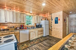 A wooden cabin kitchen with a stove, refrigerator, microwave, and wooden cabinets.