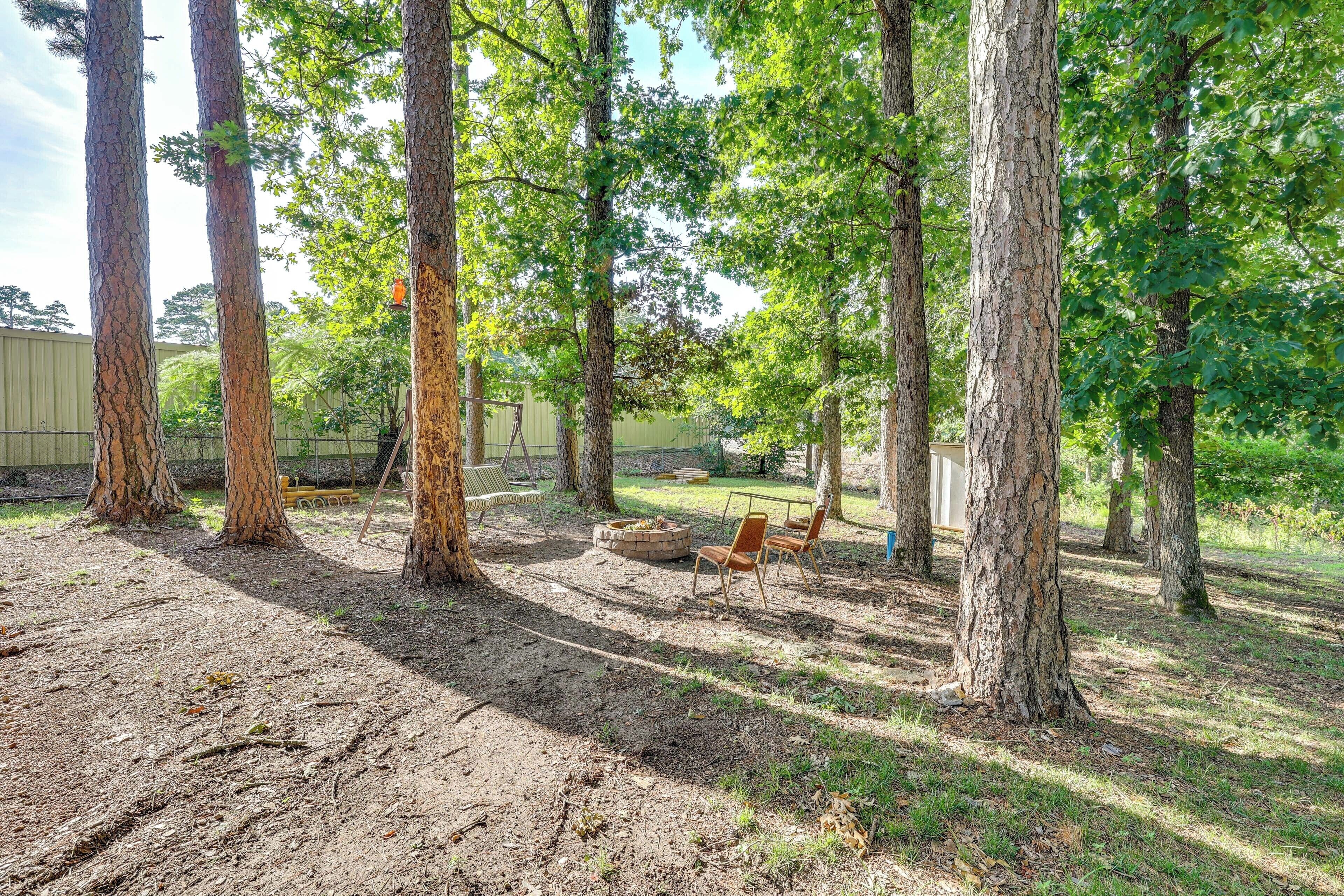 A wooded area with tall trees, a fire pit, and outdoor seating.