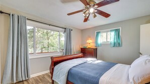 Ein Schlafzimmer mit einem hölzernen Bett, einem Deckenventilator, einem Fenster mit Vorhängen und einem Nachttisch mit Lampe.