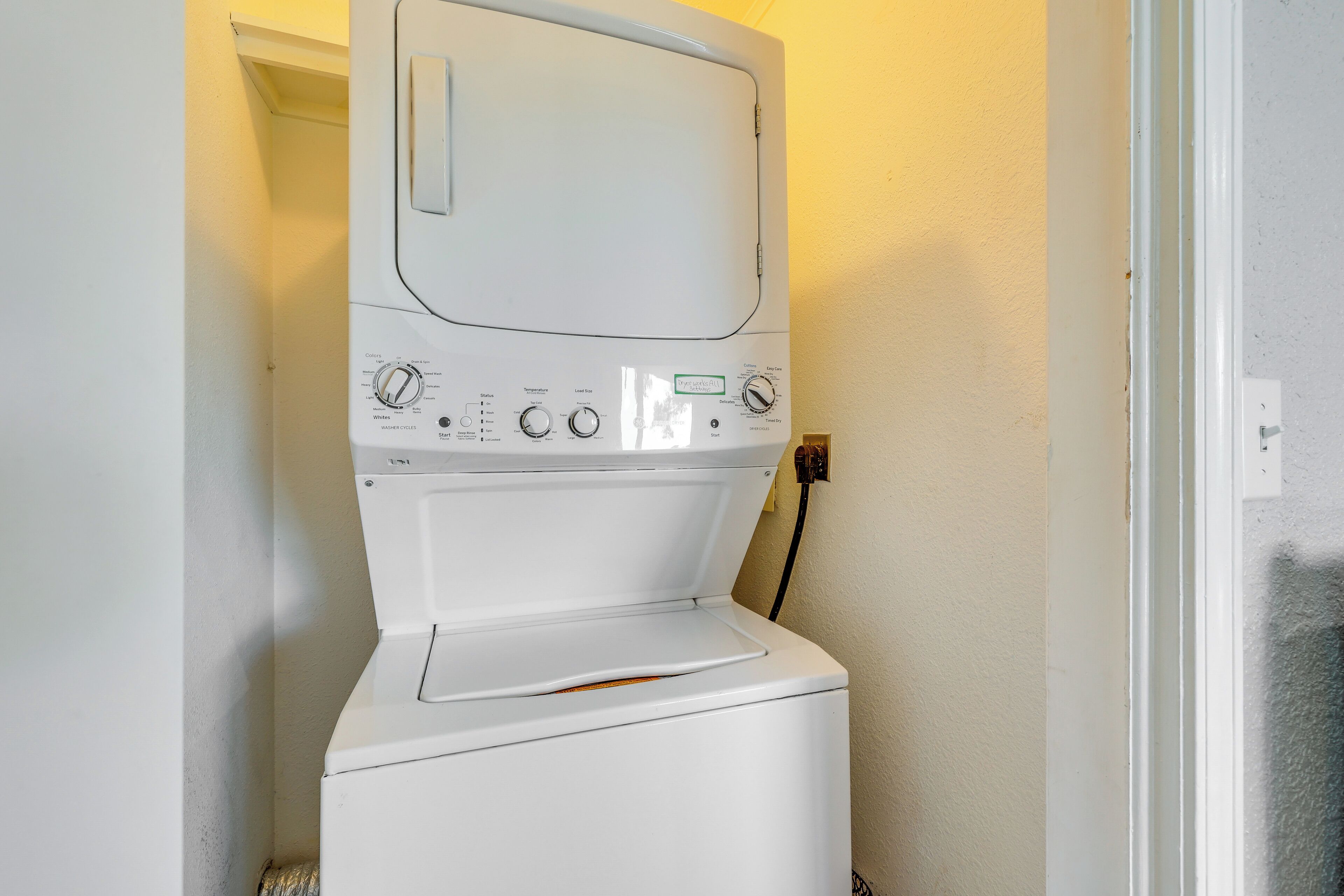 Eine Waschmaschine mit Frontlader in einem Waschraum, an der Wand weiß und eine Tür rechts.