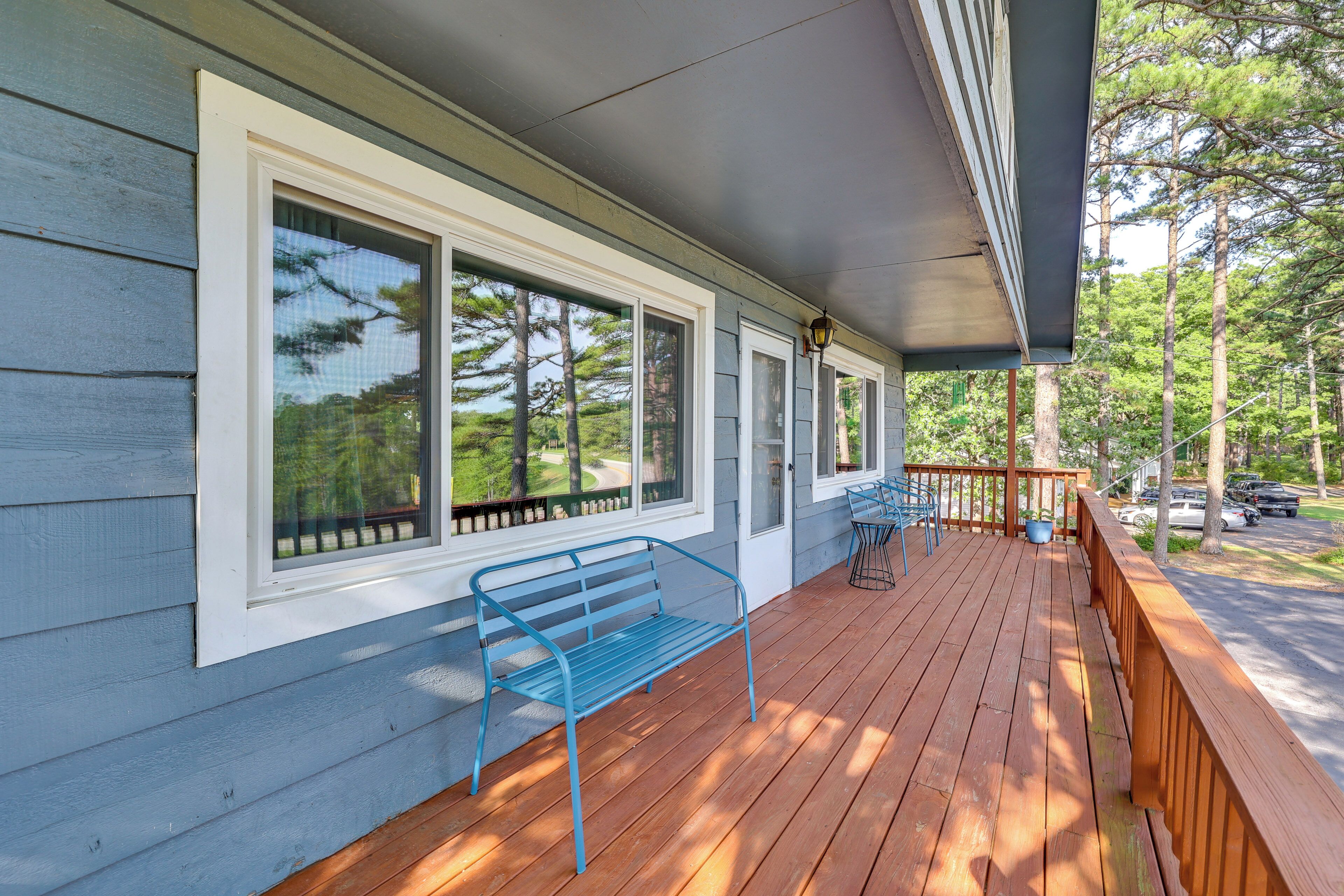 A covered porch with a blue bench, large windows, and a view of the surrounding trees.