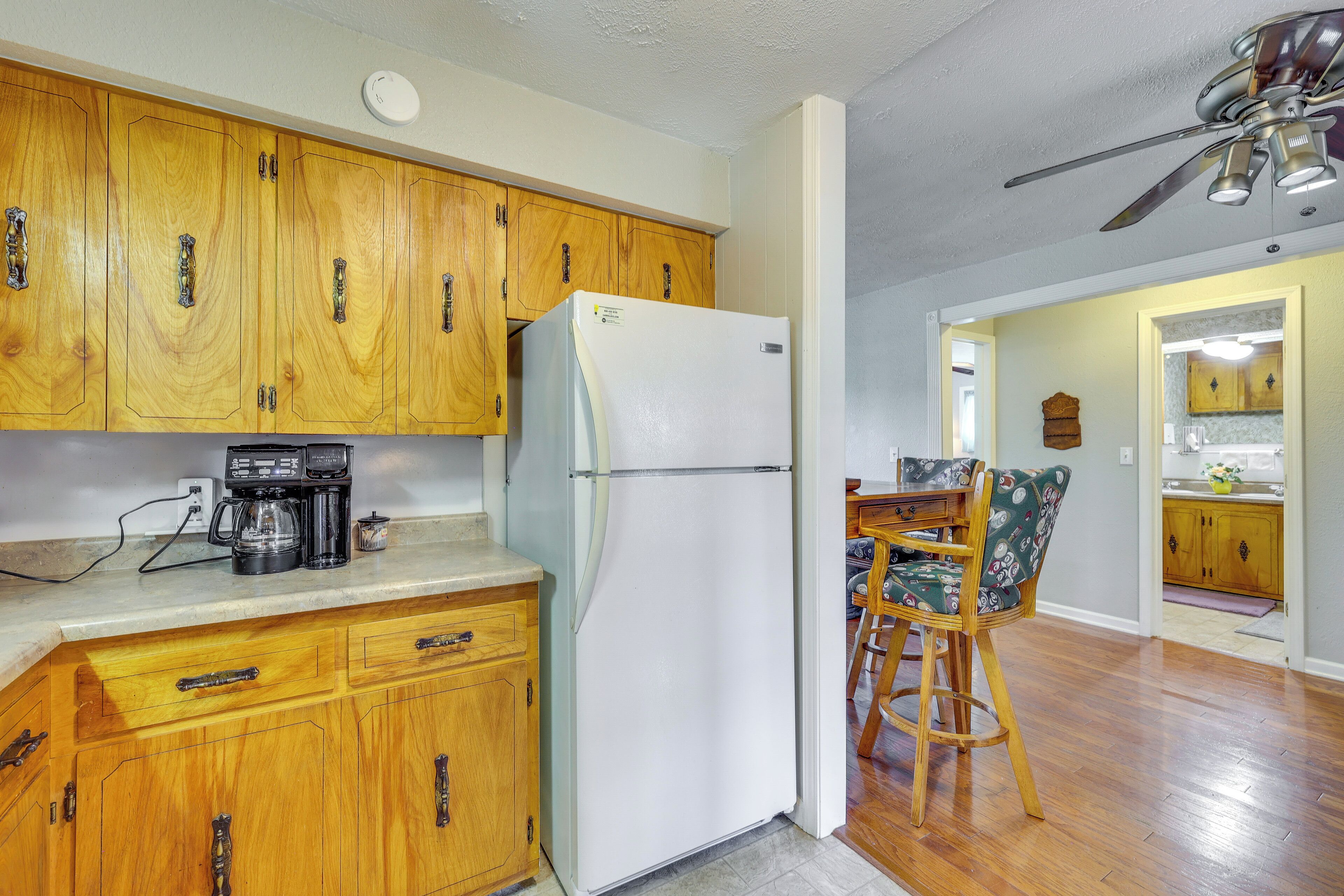 A kitchen with wooden cabinets, a white refrigerator, a coffee maker, and a dining area with a chair.