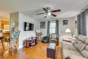A living room with a ceiling fan, a sofa, a coffee table, a TV, and a dining area with wooden cabinets and chairs. - 4 Mi to Dtwn! Ozarks Hideaway w/ Furnished Deck (Eureka Springs)